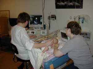 Sonographer performing an ultrasound excamination on a baby with mother present. Echocardiography by Kjetil Lenes in wikipedia Public Domain